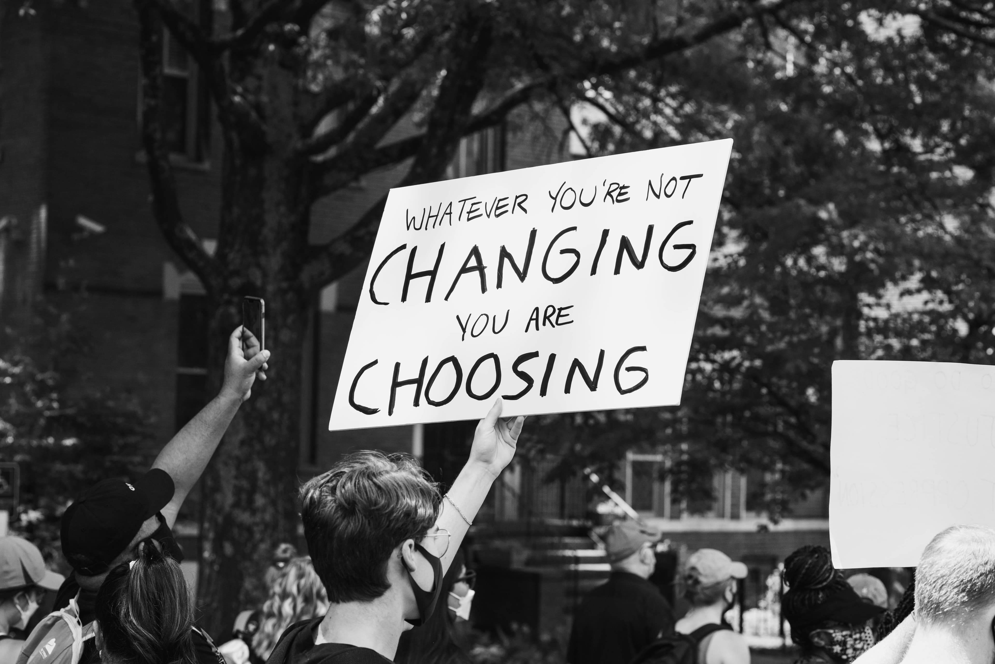 A protester holds a sign that reads Whatever you’re not changing you are choosing